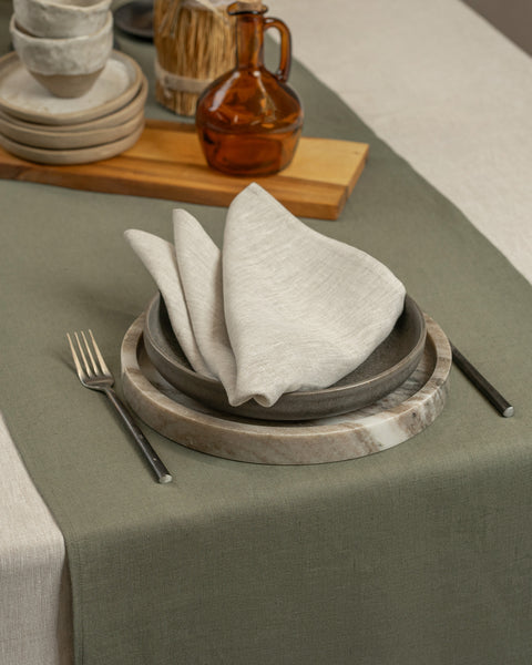 Olive green linen table runner on a neutral tablecloth with stoneware plates, layered linens, and minimalist rustic table décor.