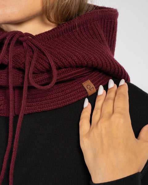 Primer plano de pasamontañas con capucha de lana merina tejida en color cereza real, con cordones ajustables y etiqueta con el logo de menique.