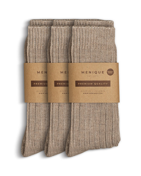 Tres pares de calcetines gruesos beige para mujer con canalé, doblados cuidadosamente y empaquetados en papel marrón de Menique con la etiqueta «Calidad Premium – Lana Merina».