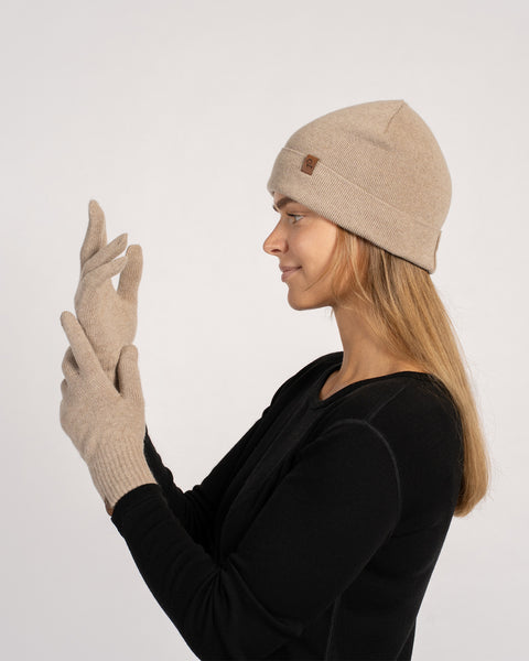 Mujer con un gorro de cachemir color beige crema y guantes cortos a juego, vista de perfil lateral, ajustándose el guante.