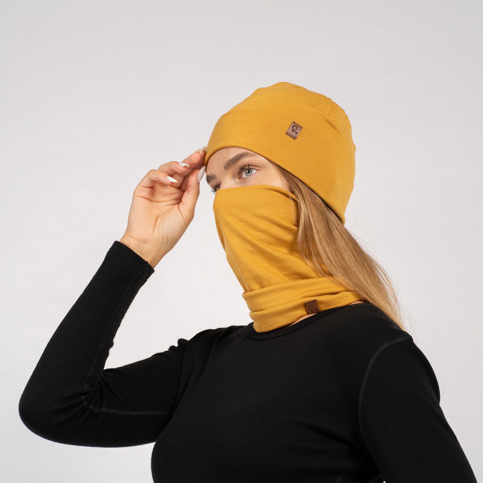 Mujer con gorro de merino amarillo y braga para el cuello, posando con camiseta negra de manga larga – vista lateral.