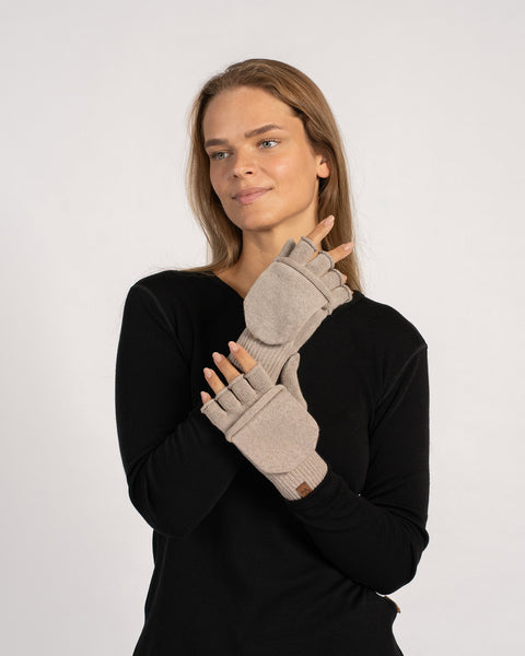 Vista de tres cuartos del modelo poniéndose un manopla convertible color crema beige con la solapa recogida, brazos ligeramente levantados.