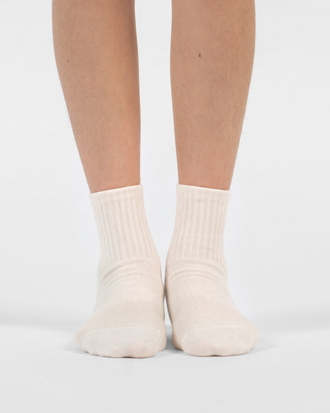 A front-facing view of a person's lower legs and feet standing side-by-side in natural off-white crew socks.