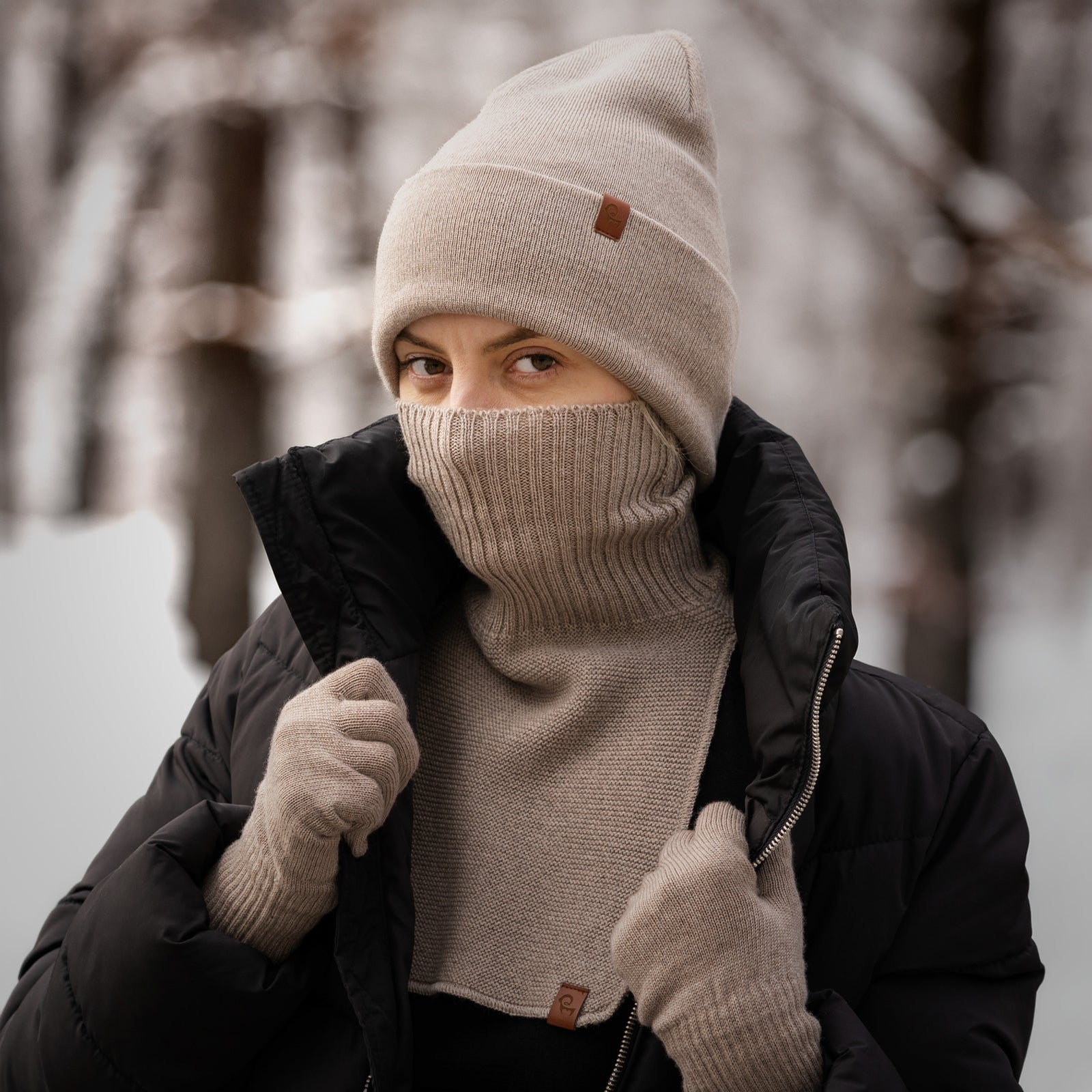 Mujer con gorro de merino beige, calentador de cuello y guantes, vestida con chaqueta de invierno al aire libre
