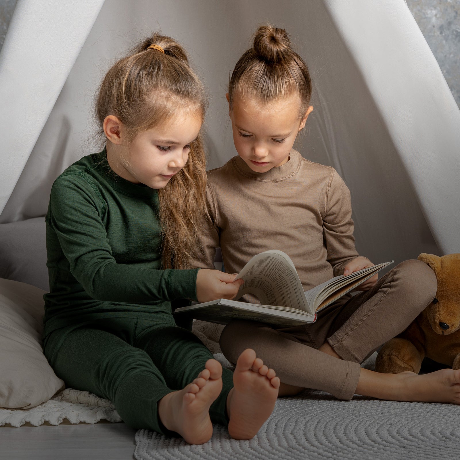 Dos niños sentados dentro de un tipi leyendo un libro.