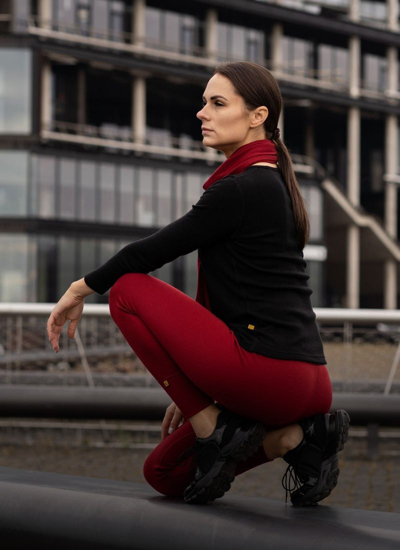 Mujer con camiseta negra y pantalones rojos agachada frente a un edificio moderno.