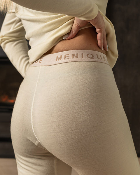 Los pantalones de lana merina tienen un color natural y están hechos de una tela lisa y suave. Tienen un corte recto en la pierna y una banda elástica. La cintura es de un color más claro y contrastante. No tienen bolsillos visibles ni adornos.