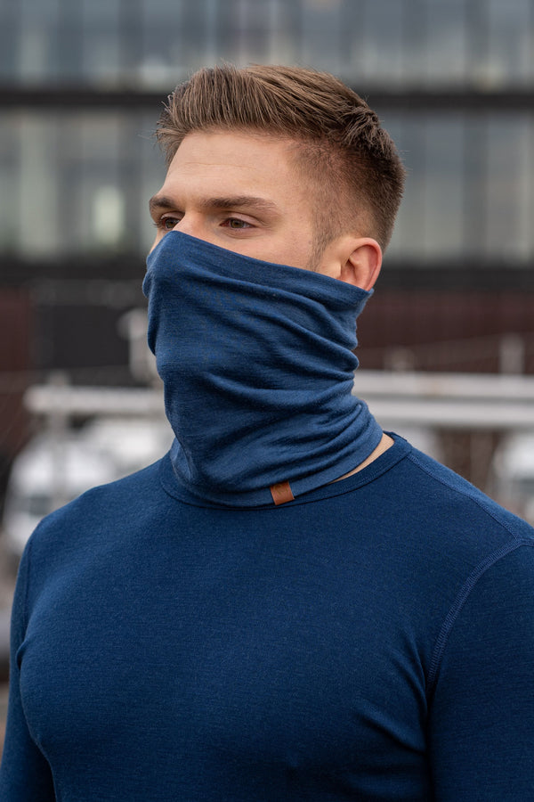Un hombre lleva el braga de cuello unisex de mezclilla de menique. Está al aire libre, vistiendo una camiseta de manga larga de merino del mismo color.